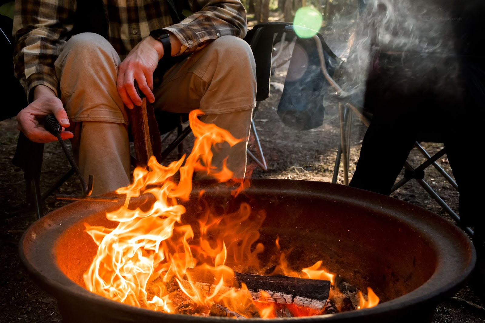 Man stoking the flames in a fire pit near Chipeta Lodge Resort + Spa