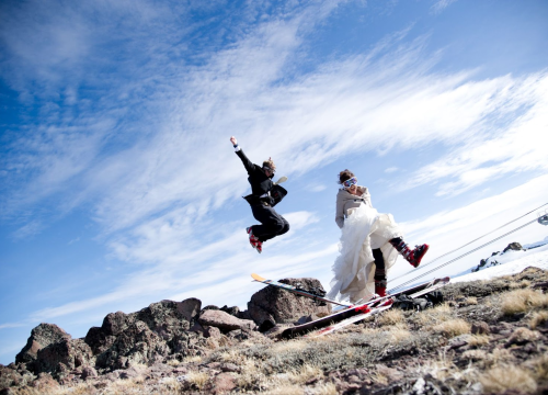 Bride and Groom in wedding outfits plus ski boots celebrating on a rocky summit near Chipeta Lodge Resort + Spa