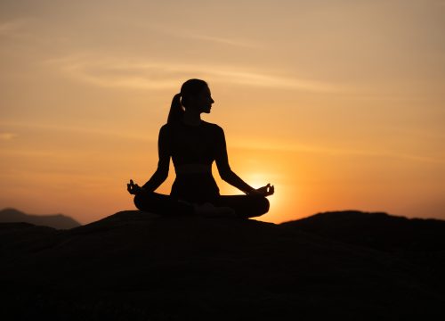 Silhouette of a person meditating in a seated pose on rocks at sunset near Chipeta Lodge Resort + Spa