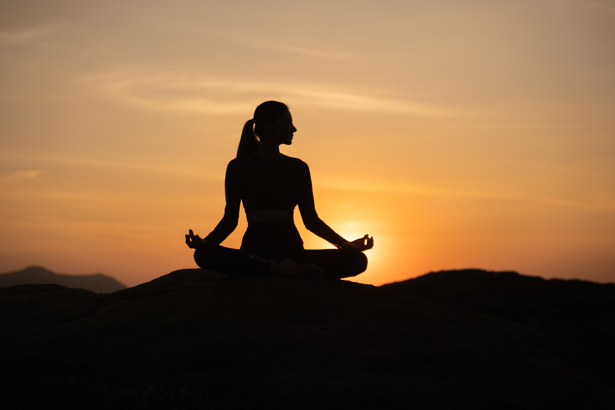 Silhouette of a person meditating in a seated pose on rocks at sunset near Chipeta Lodge Resort + Spa - Chipeta Lodge Resort + Spa Silhouette of a woman at a yoga festival atop mountain peak at sunset near Chipeta Lodge Resort + Spa