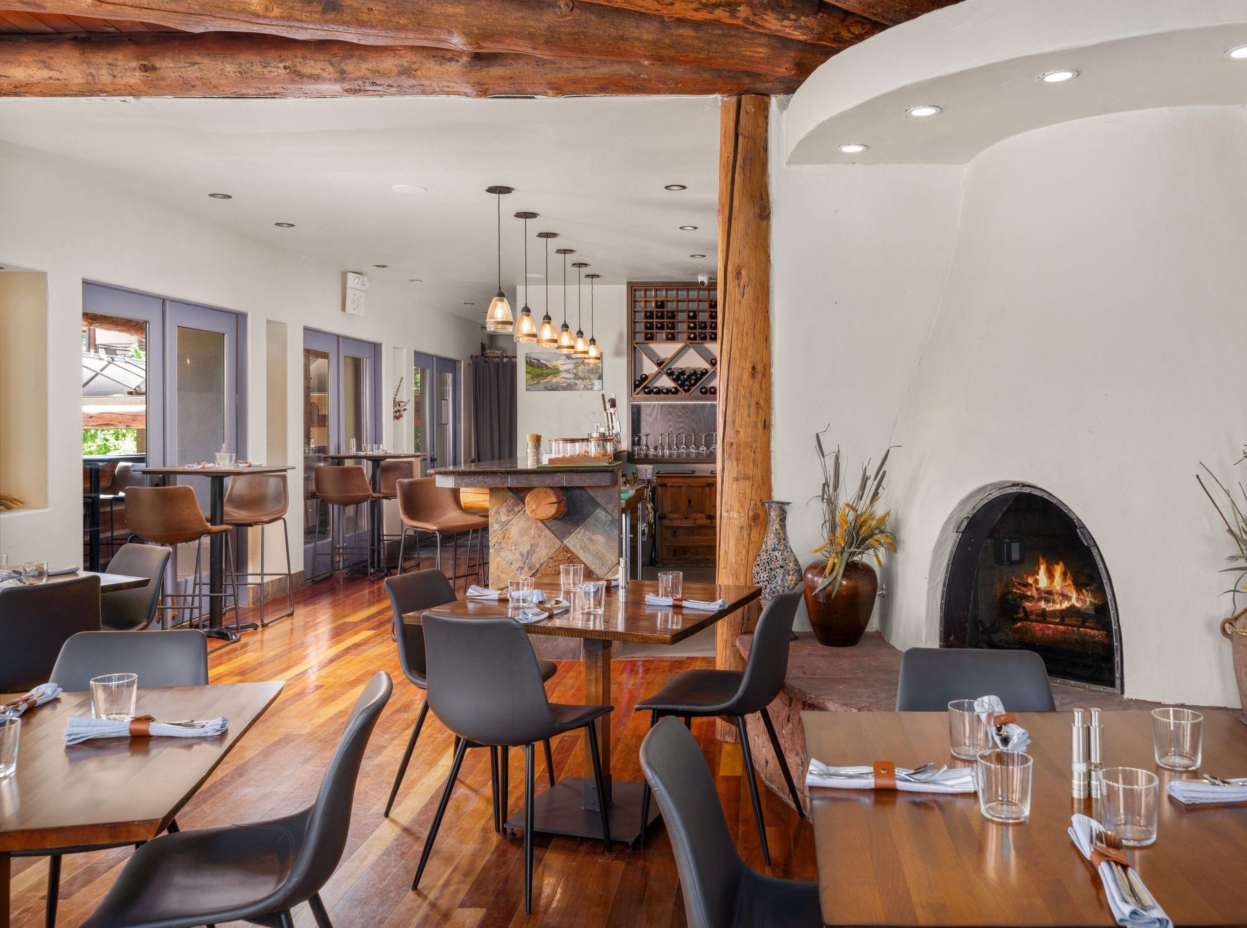 Cozy restaurant interior with exposed wooden beams, curved white wall, and a lit fireplace with seating nearby.