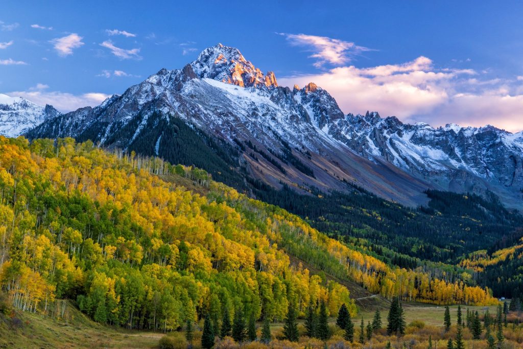 image - Chipeta Lodge Resort + Spa Snow-capped mountain range with a golden aspen forest below and a blue sky above at dusk/dawnlight.