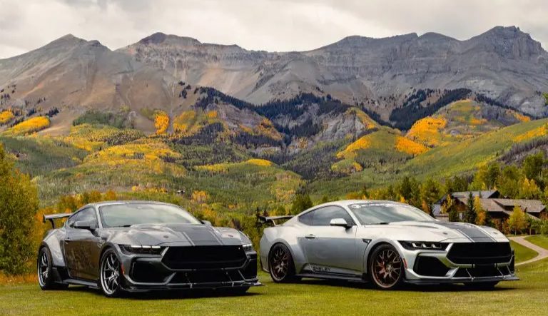 image - Chipeta Lodge Resort + Spa Two high-performance sports cars parked on a grassy field with autumn trees and mountains in the background.