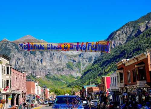Telluride Blues & Brews Festival banner across a sunny mountain town street beneath a blue sky.