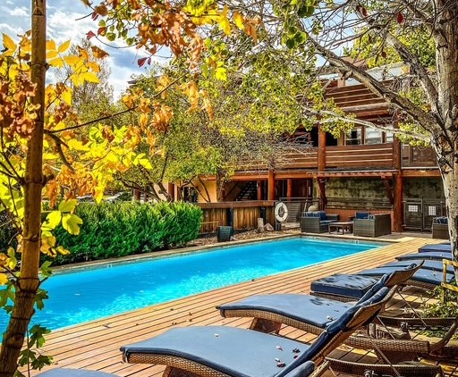 image - Chipeta Lodge Resort + Spa Outdoor pool area with blue water, wooden deck, lounge chairs, and a two-story wooden building framed by autumn trees.